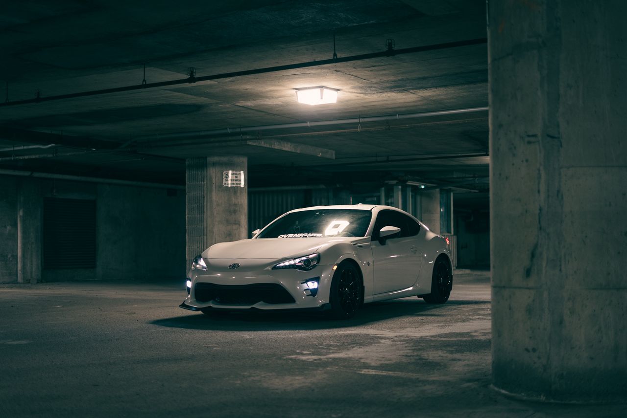 A modern white sports car parked in a dim garage, exuding a mysterious ambiance.