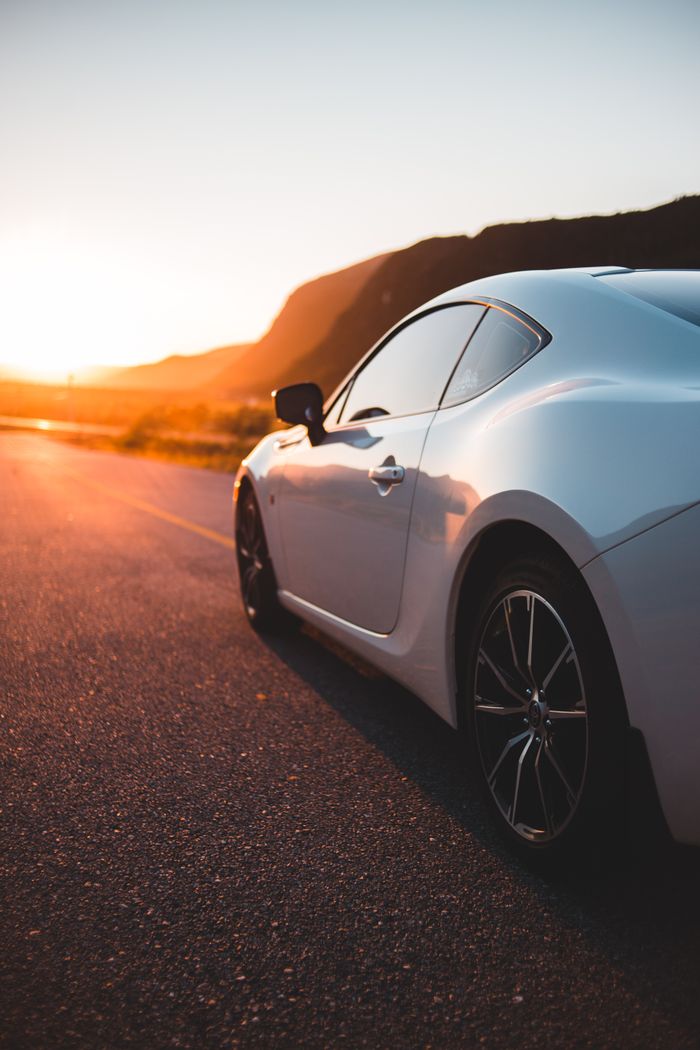 Shiny white coupe automobile on paved route in bright light of sunset in mountains
