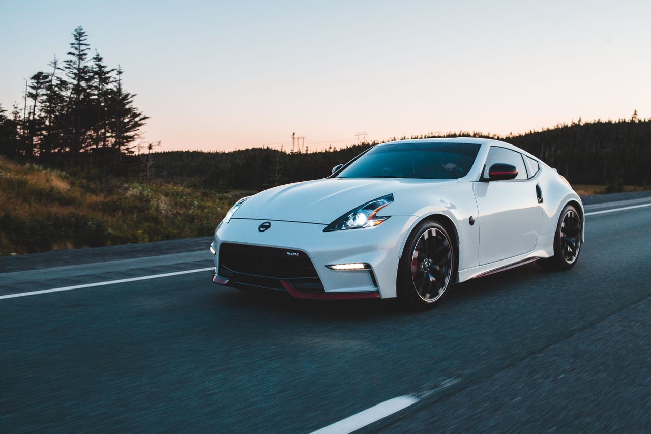 Expensive white vehicle driving on asphalt roadway with marking lines along grassy terrain against cloudless sky in nature in daytime